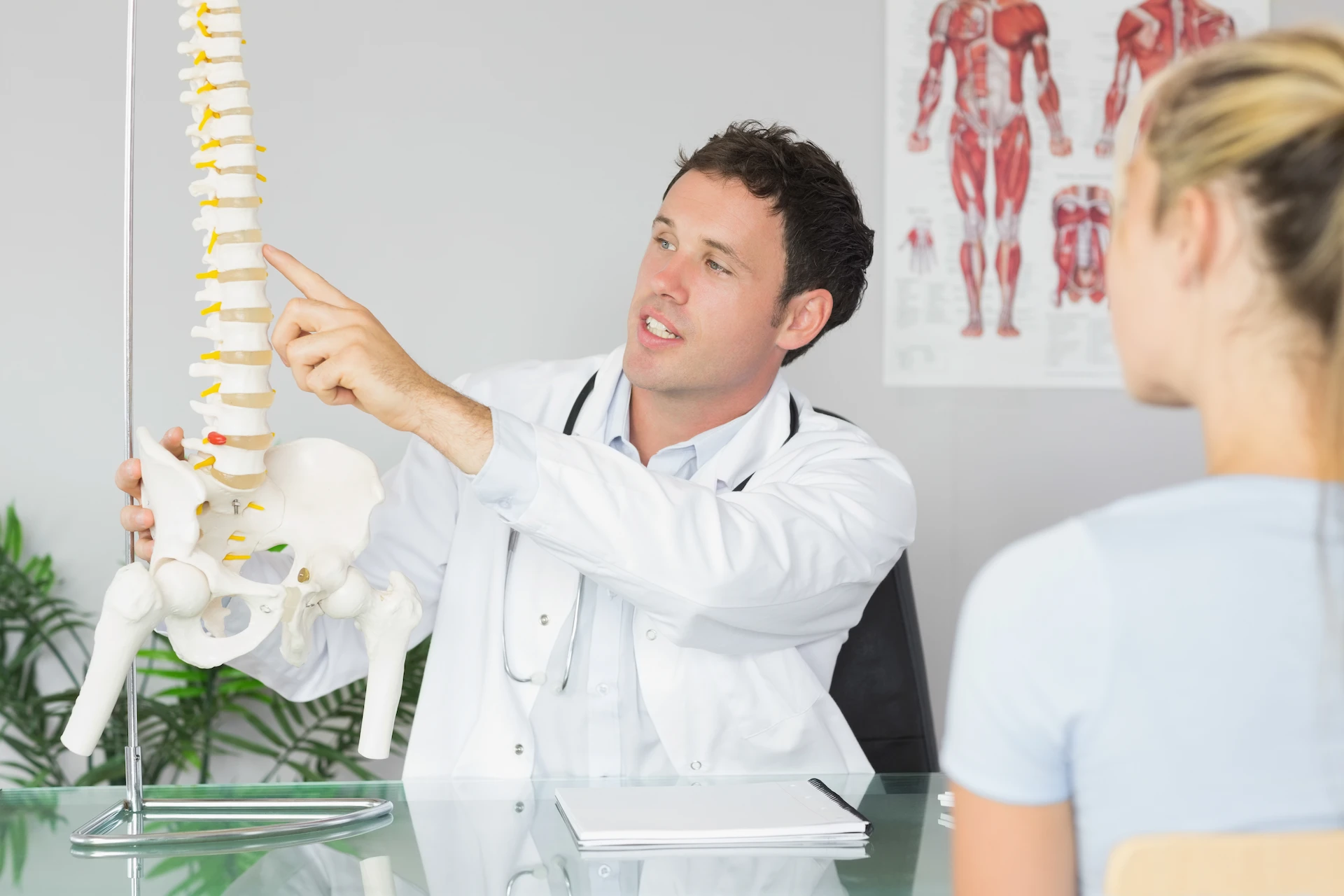A fellowship-trained specialist pointing to a spine model during a patient consultation discussing the benefits of a targeted spinal injection.