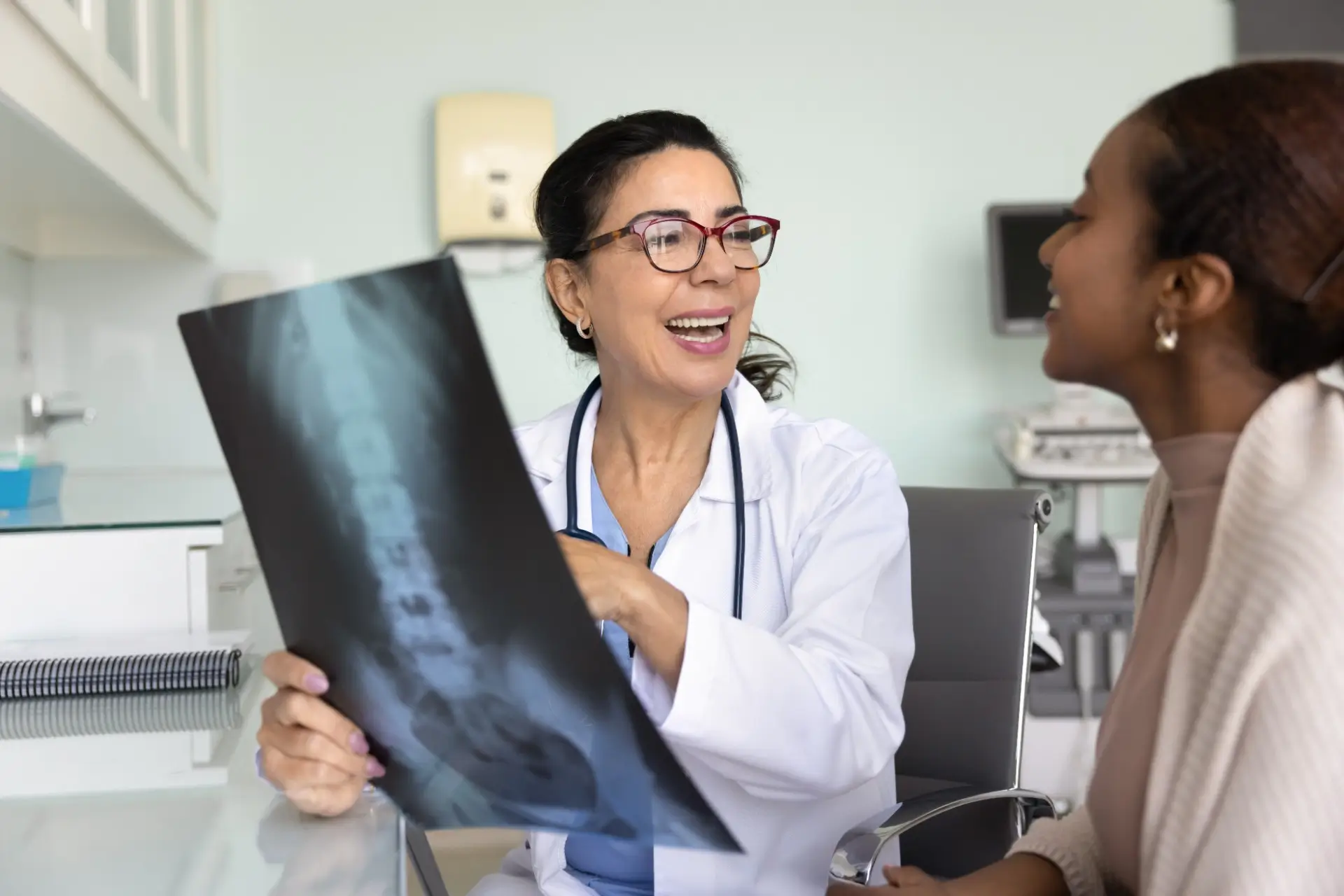 A female pain doctor reviewing a spinal X-ray scan during a consultation to explain personalized pain management services to a patient at Innovative Pain Care Center.